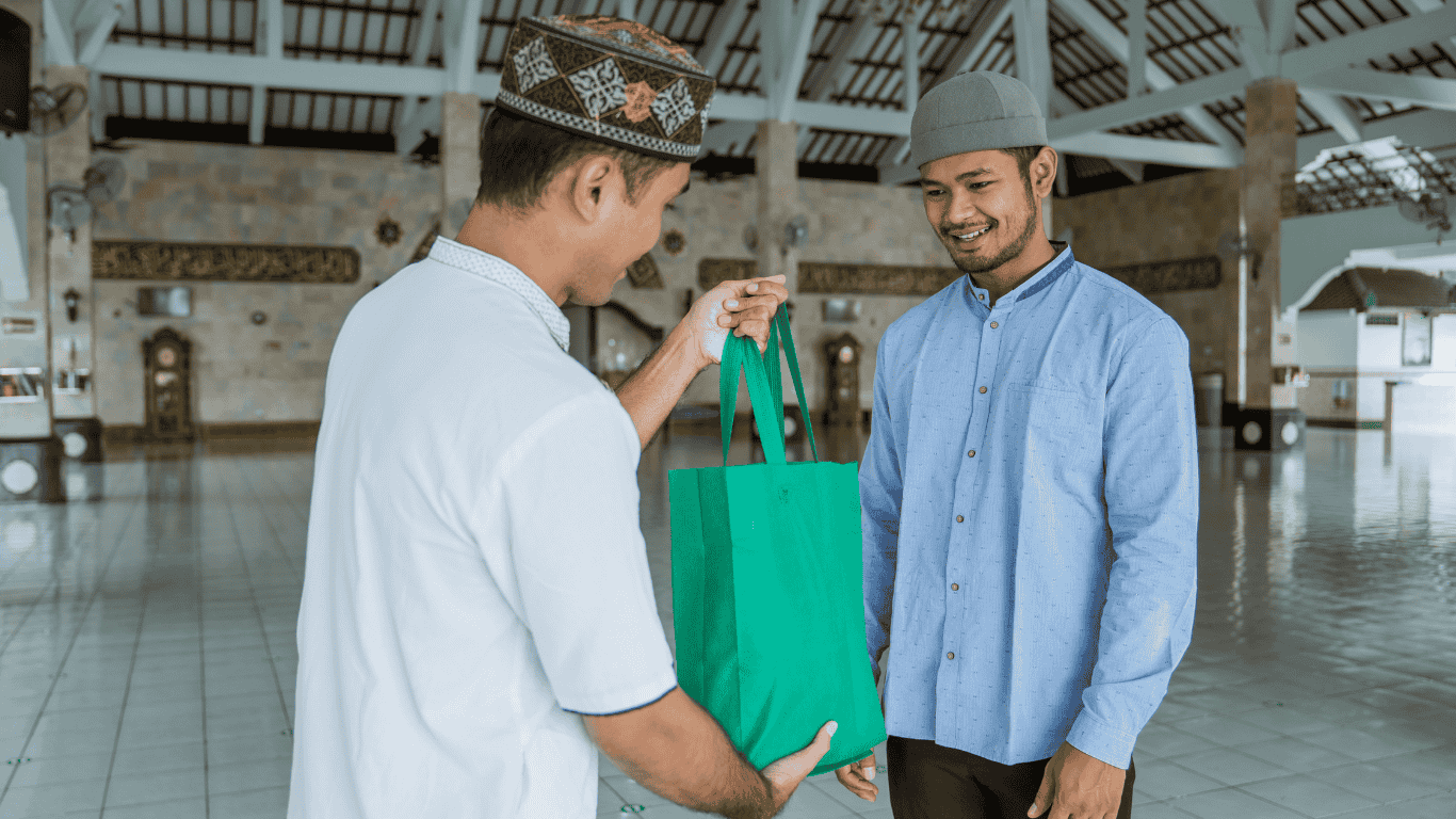 Seorang pria sedang memberikan hadiah kepada temannya, keduanya tersenyum bahagia, menggambarkan semangat beramal shalih di usia muda sesuai pesan Surat At-Tin.