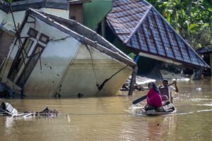 gambar orang menaiki perahu dengan latar belakang banjir Sumatera dan rumah rusak